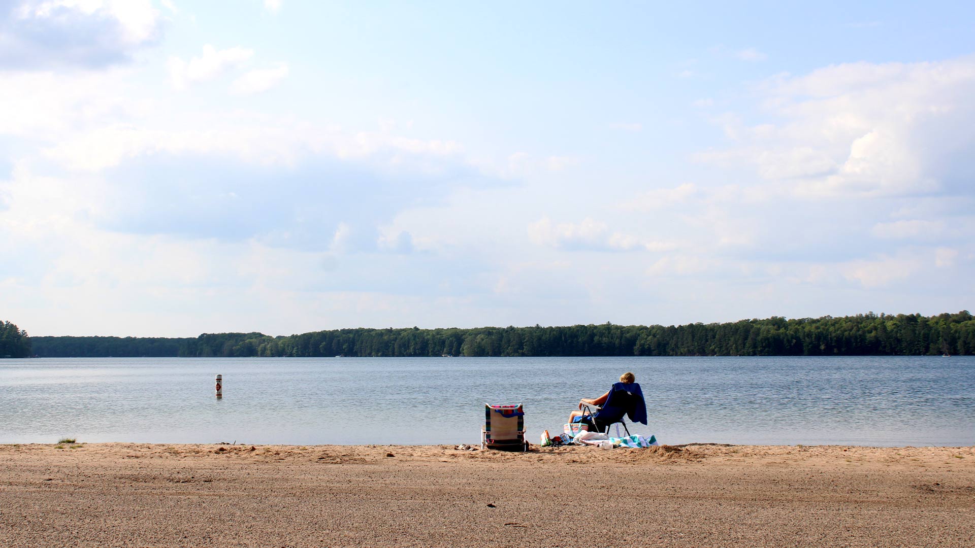 person relaxing on beach chair in front of large lake flanked with trees