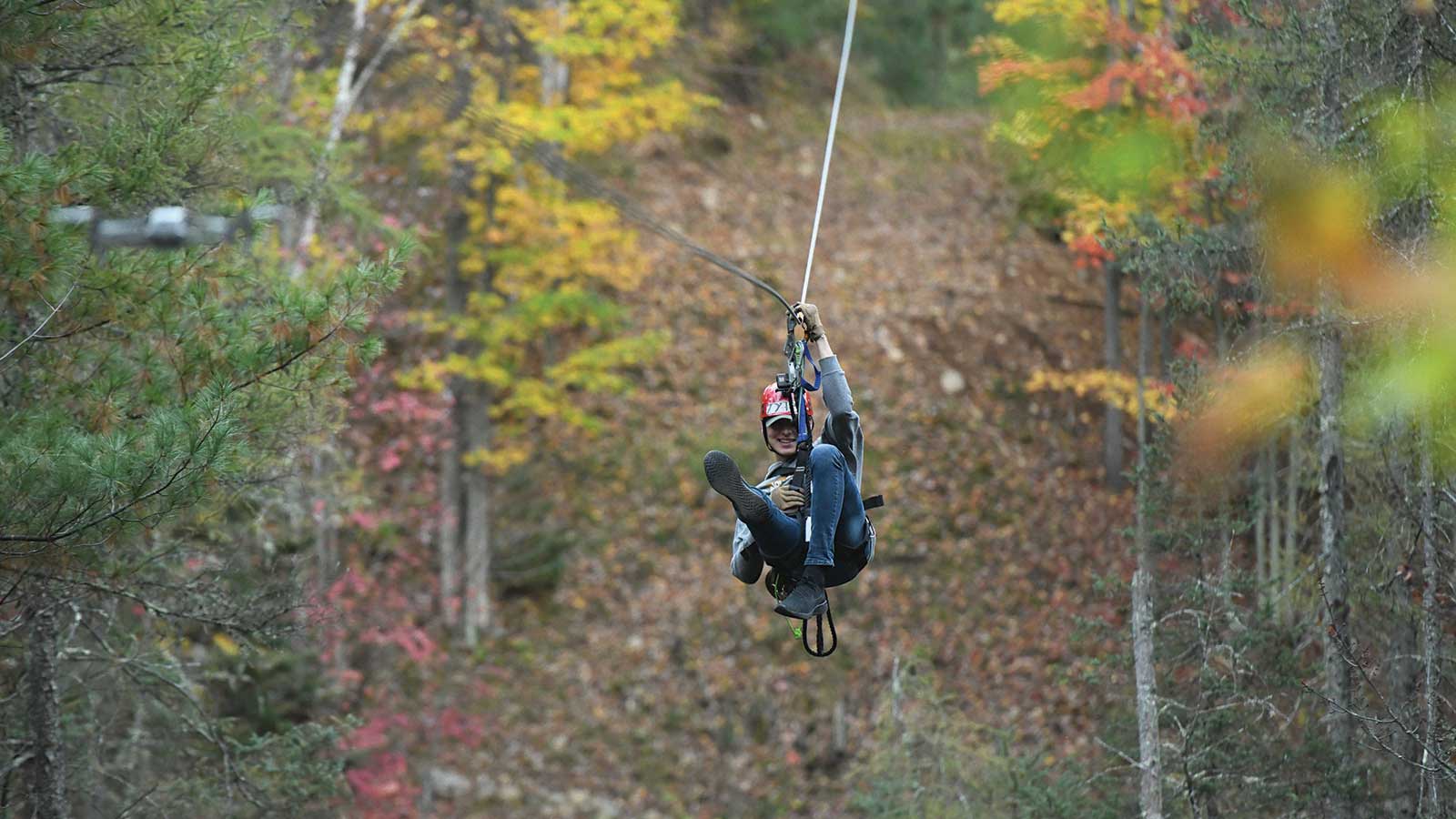 Zip liner zipping between fall trees at Northwoods Zip Line Adventure Tours