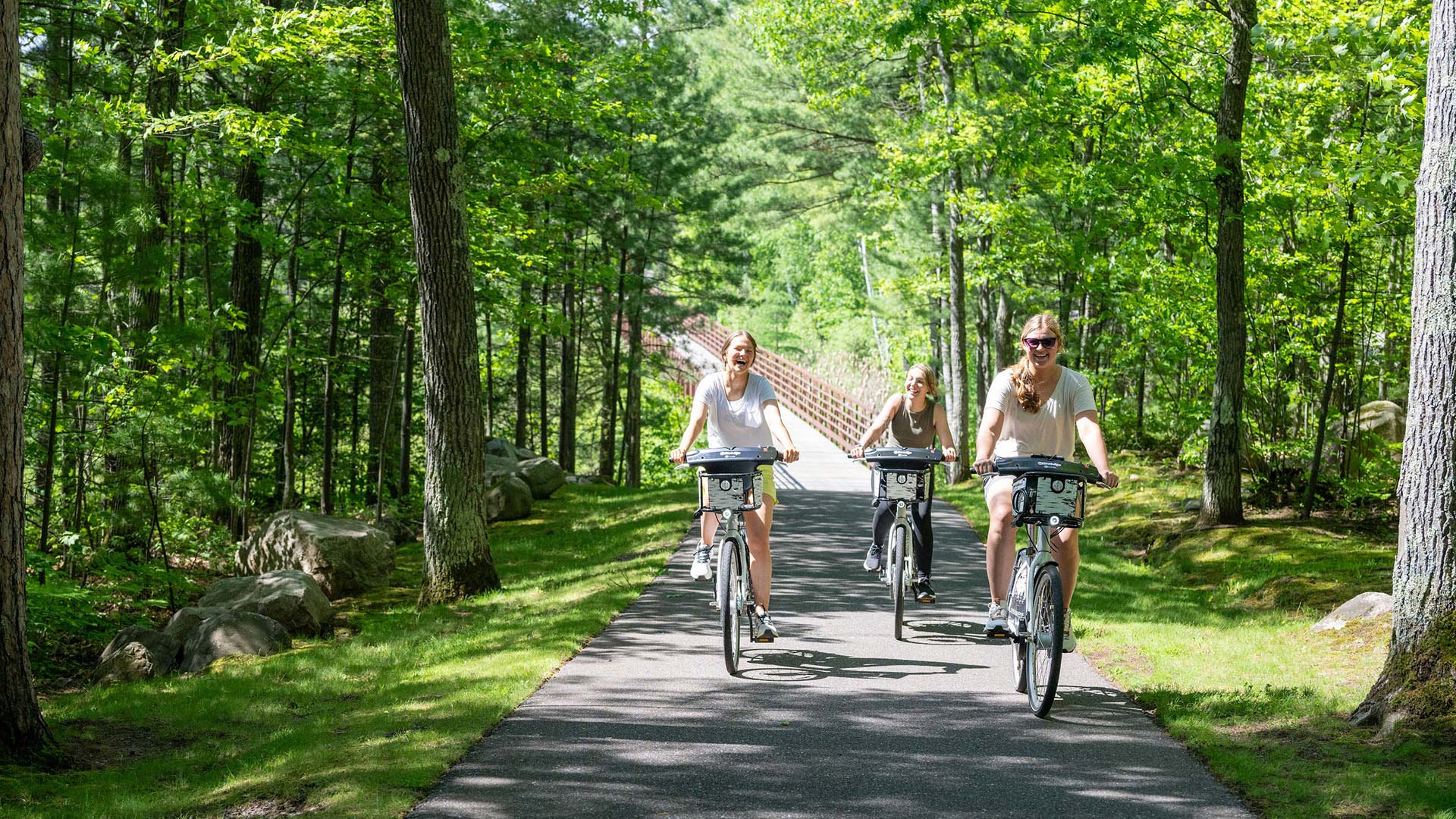 Girls riding e-bikes on a paved trail in summer
