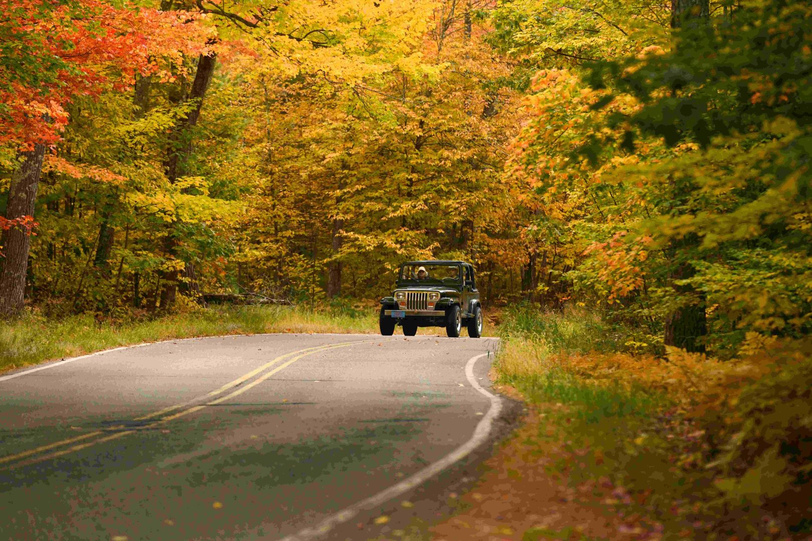 Jeep traveling along Rustic Road lined with fall color in Boulder Junction