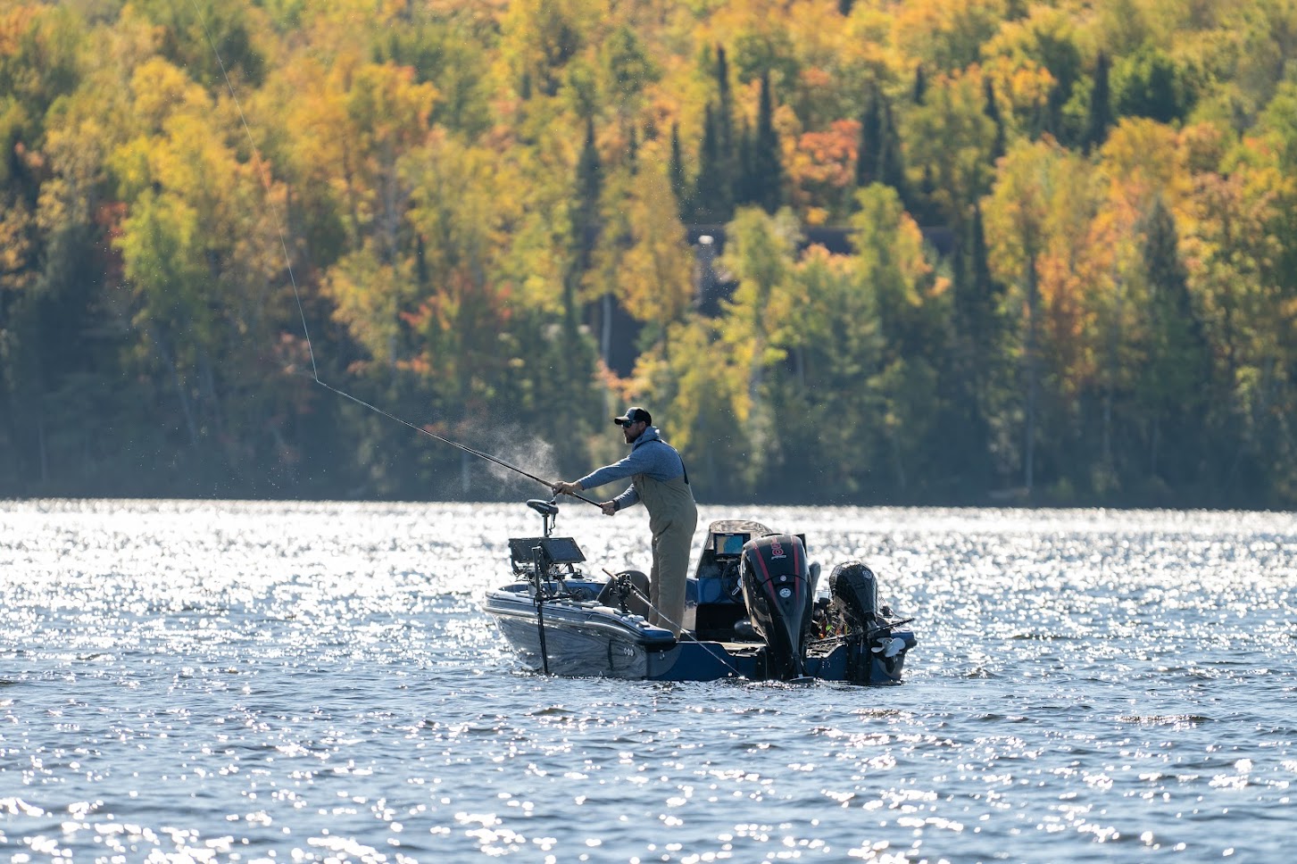 Man casting out his fishing line from his boat on Crab Lake with fall colored trees in the distance