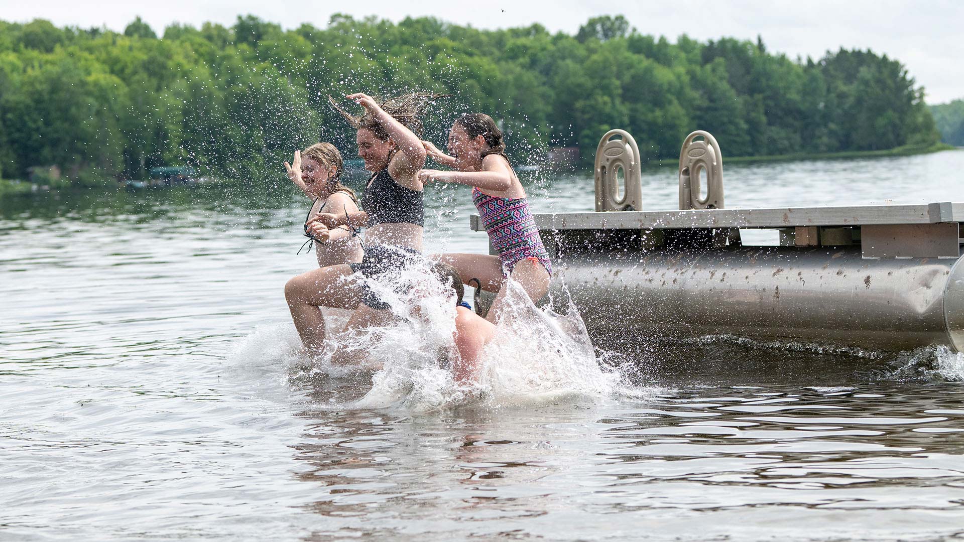Girls jumping off of a floating dock, splashing into water in front of Lynx Lake Resort